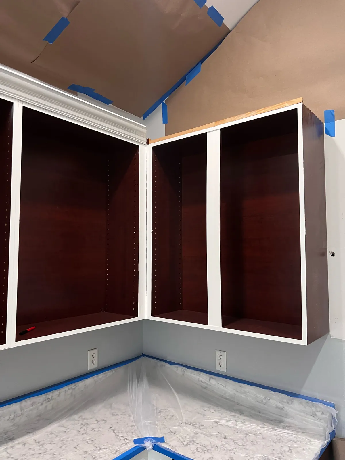 Cabinets being refinished from dark cherry to white with the openings masked off