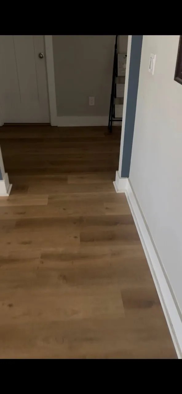 Warm wood-look luxury vinyl plank flooring running down a hallway with white baseboards