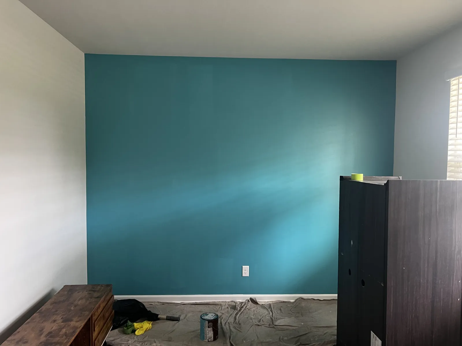 Bedroom mid-repaint with a bold teal accent wall and drop cloths protecting the floor