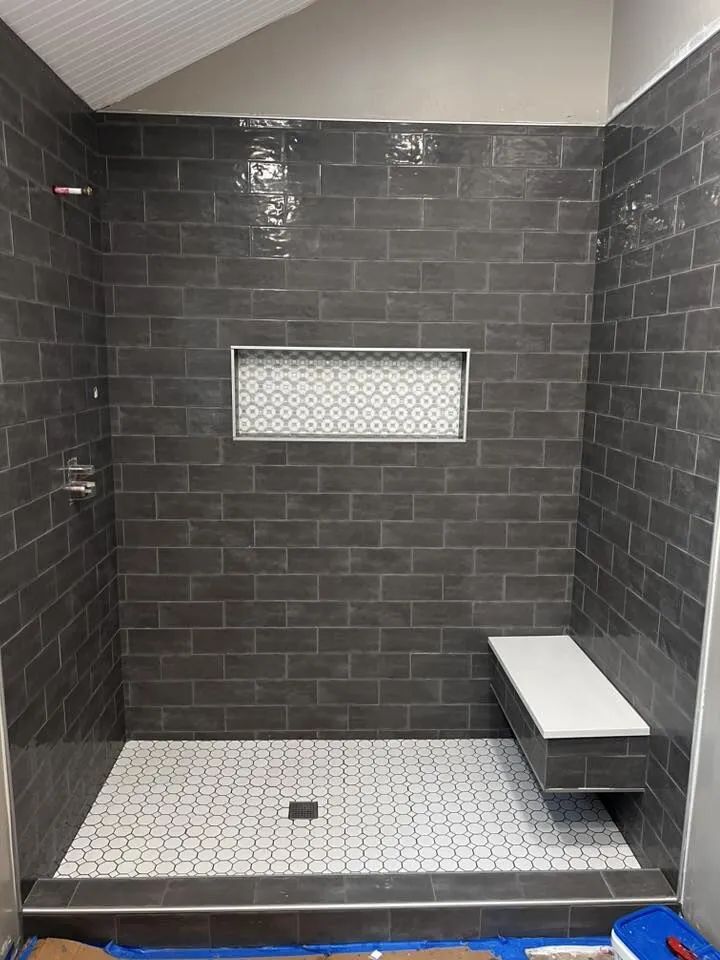 Charcoal subway tile walk-in shower with white hexagon floor, niche, and floating bench