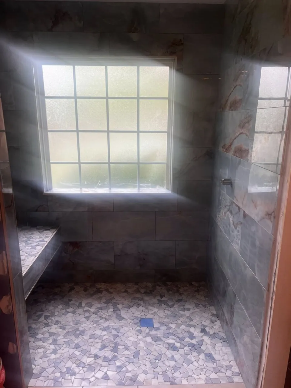 Dark marble large-format tile shower with mosaic pebble floor in progress