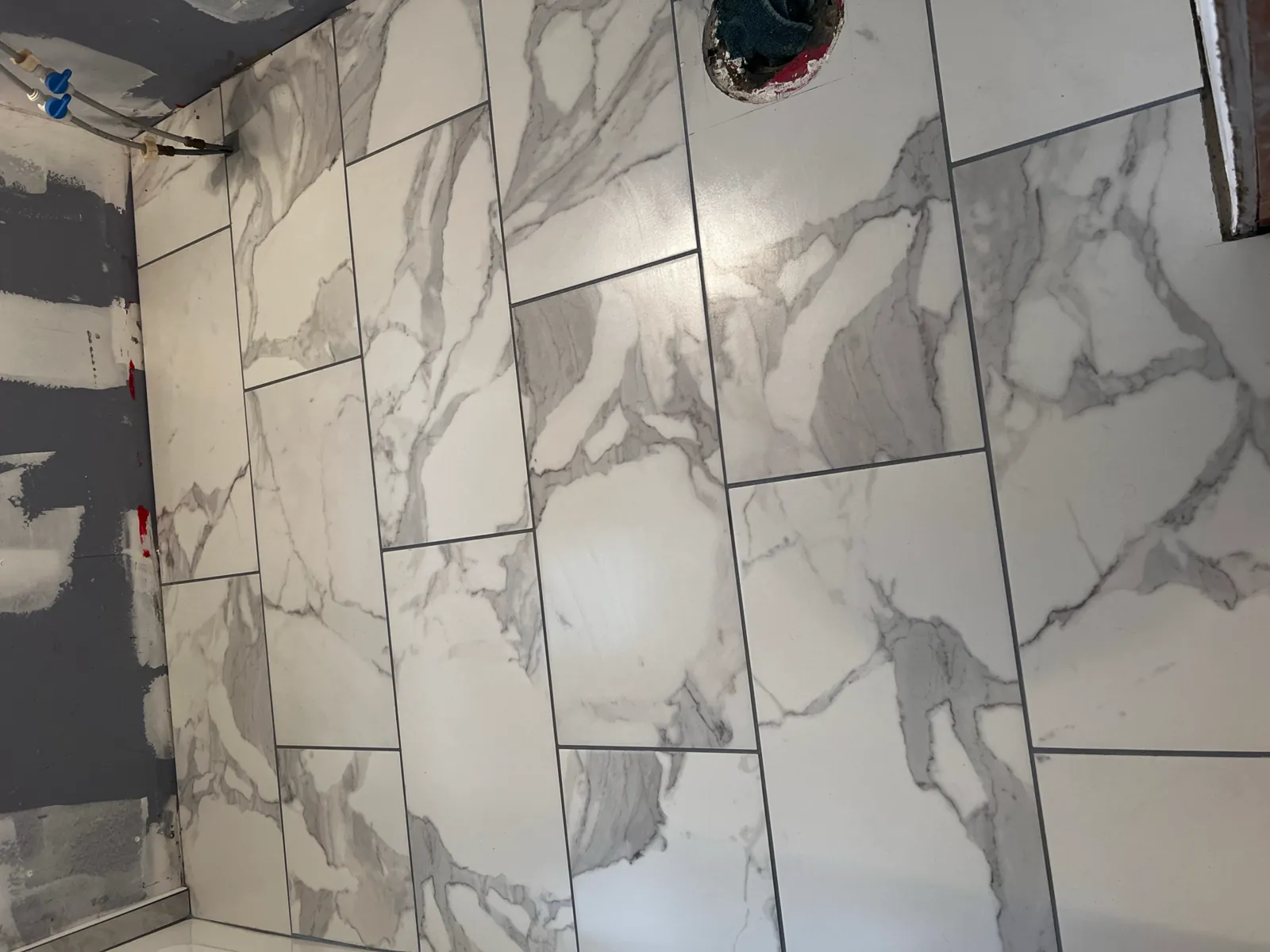 White marble large-format porcelain shower walls being tiled around the valve rough-in
