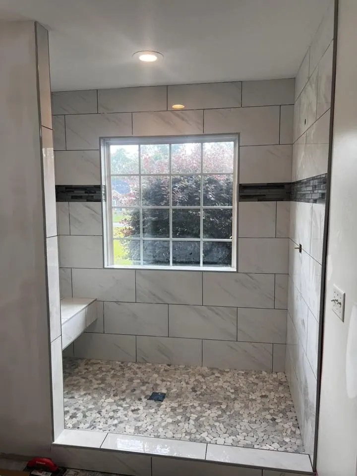 Finished white marble-look tile shower with window, bench, and pebble floor