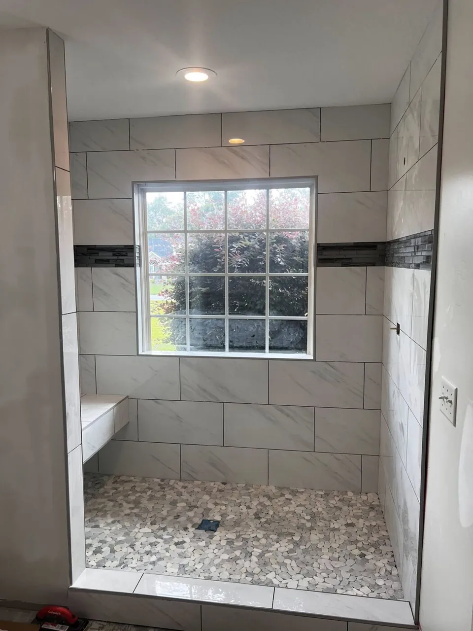 White marble-look tile shower with glass-mosaic accent band and corner bench