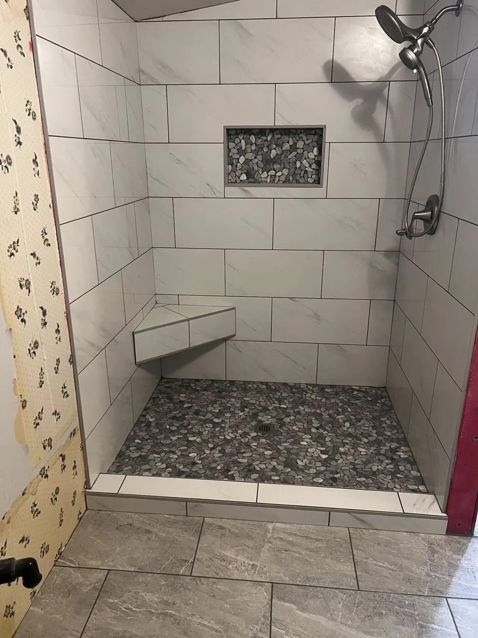 White marble subway tile shower with pebble floor, corner bench, and recessed niche