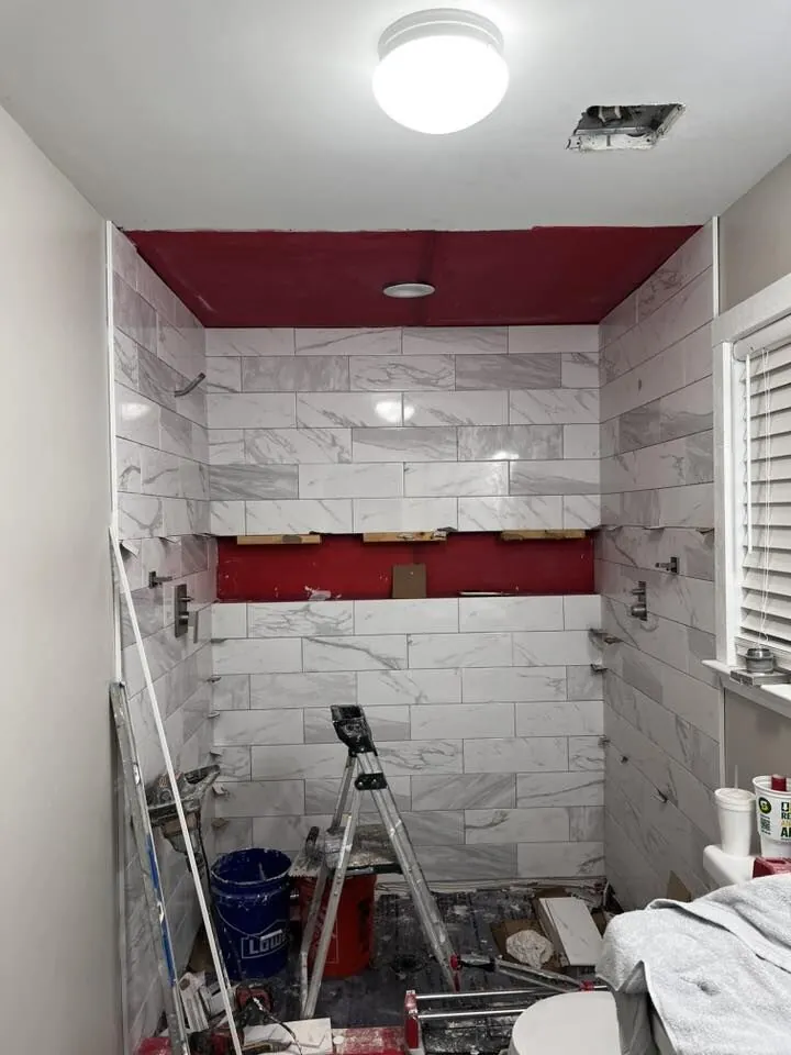 White marble subway tile shower walls going up over red waterproofing membrane